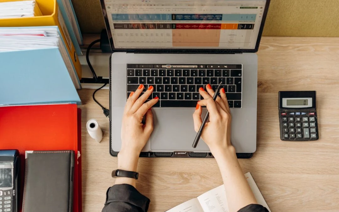 An accountant maintains books on her laptop with a calculator placed next on her table.